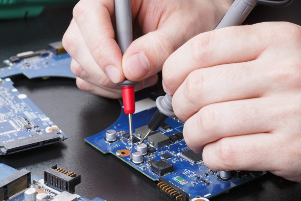 fachowiec naprawia laptopa, robiąc pomiar napięcia na elementach elektroniki